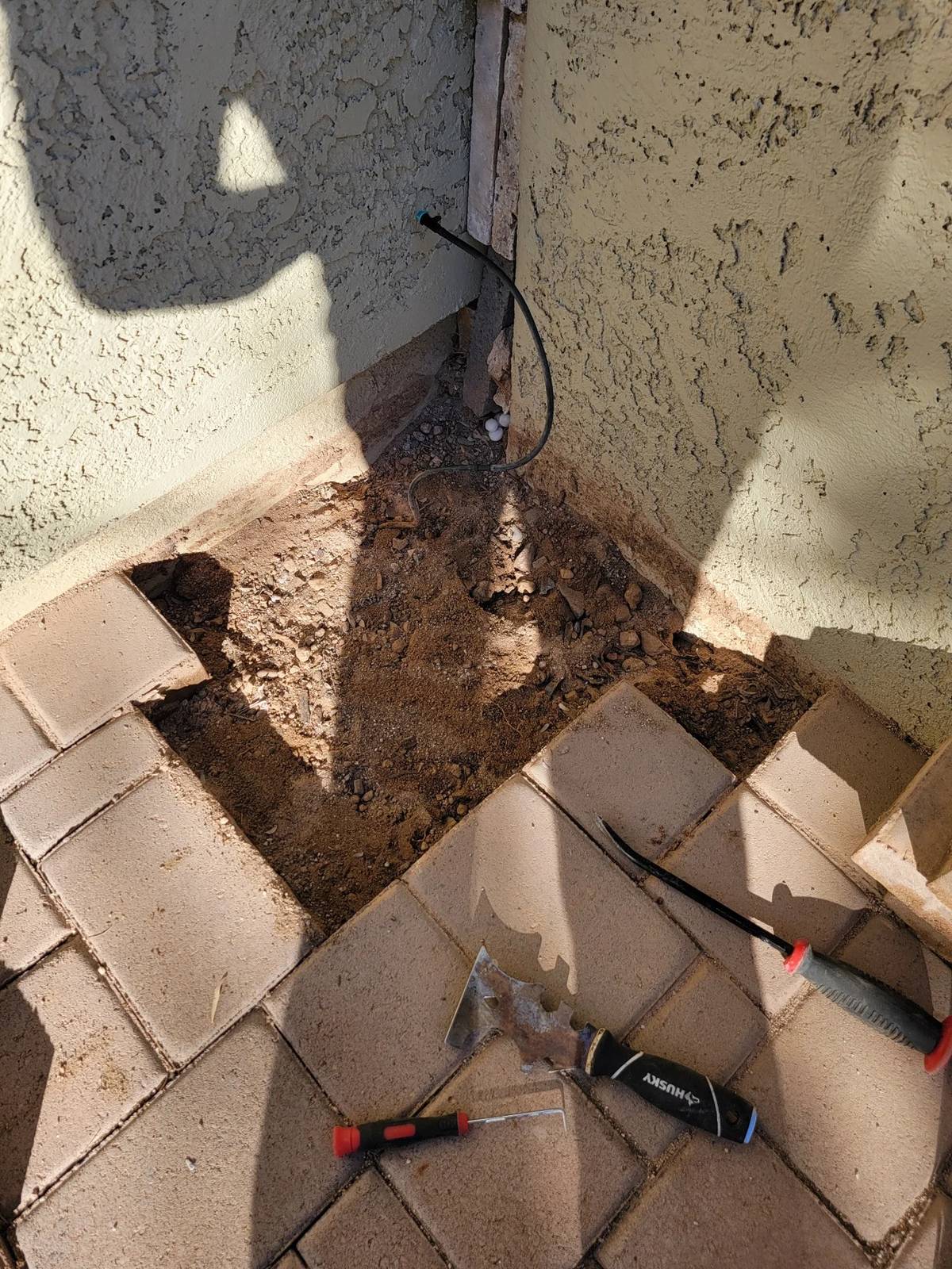 Lifted pavers and exposed base during a localized repair beside a stucco wall